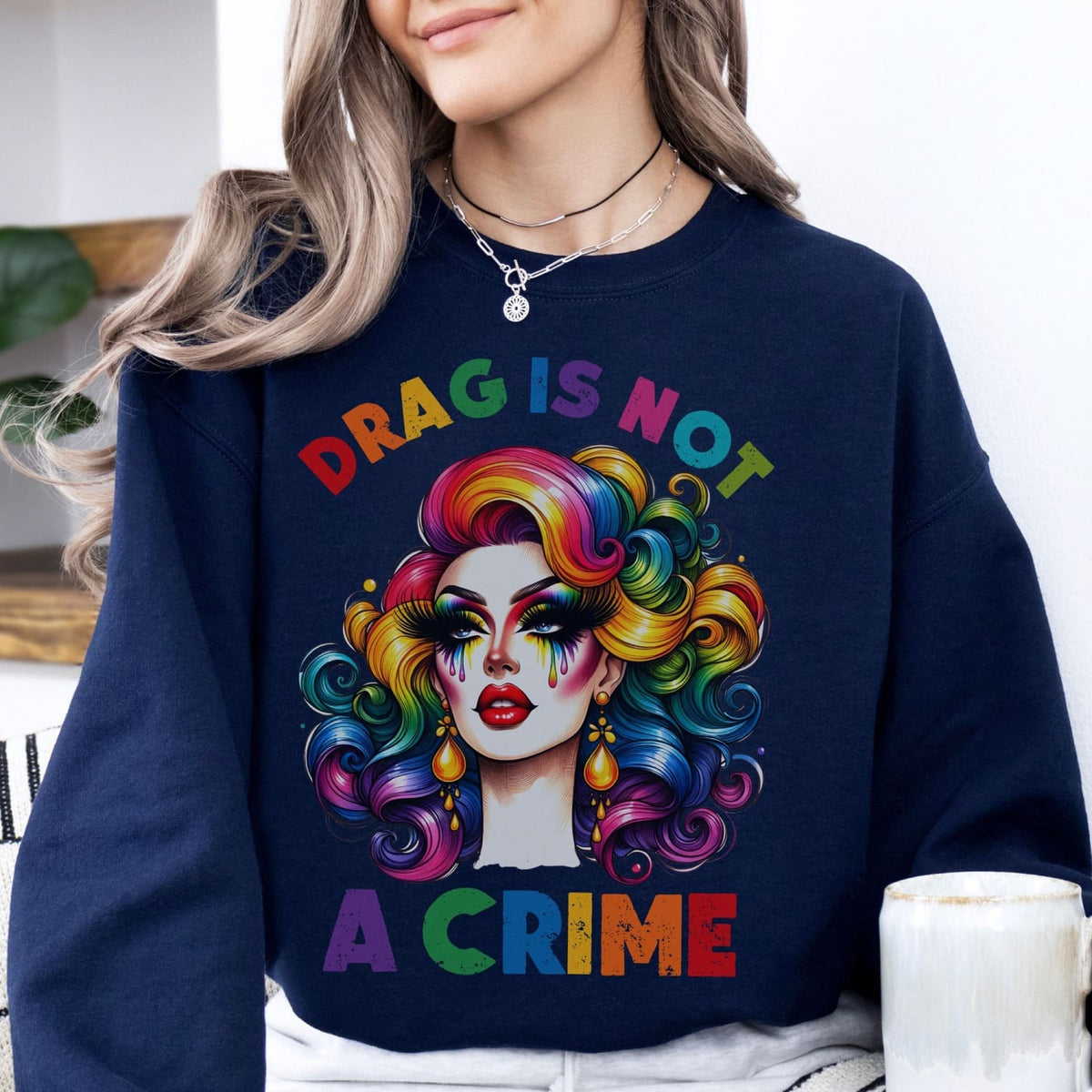 Person wearing a navy sweatshirt with drag queen graphic and 'Drag is Not a Crime' text.