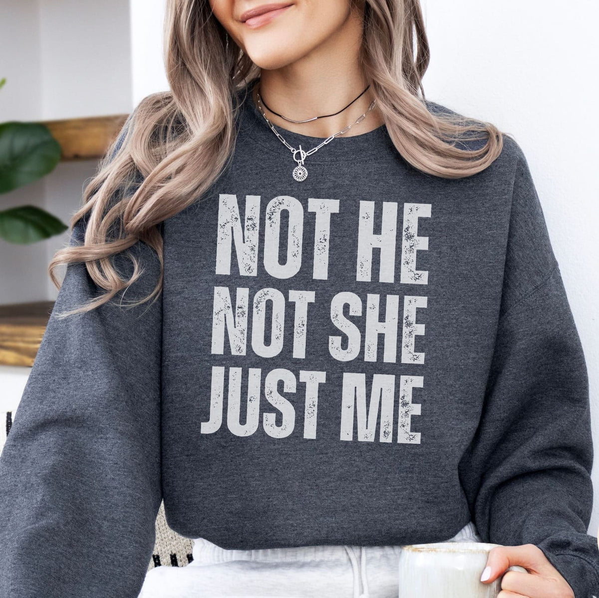 Person wearing a dark gray non binary sweatshirt with 'Not He, Not She, Just Me' text.