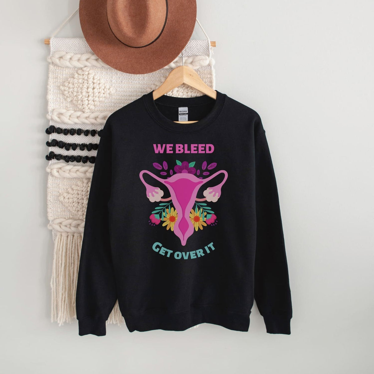 Black feminist sweatshirt with graphic design and text on a hanger against a white wall.