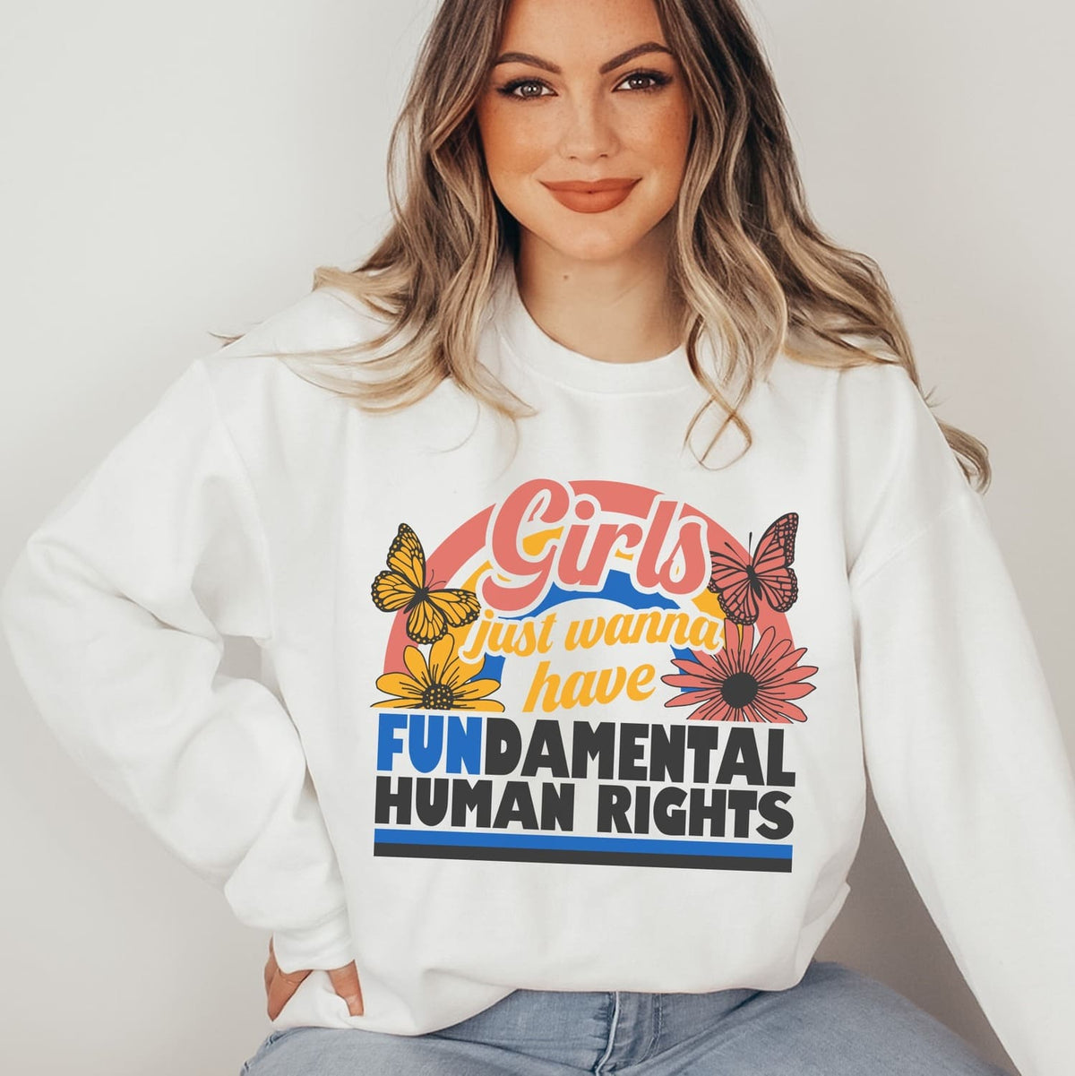 Person wearing a white feminist sweatshirt with a colorful graphic and text.