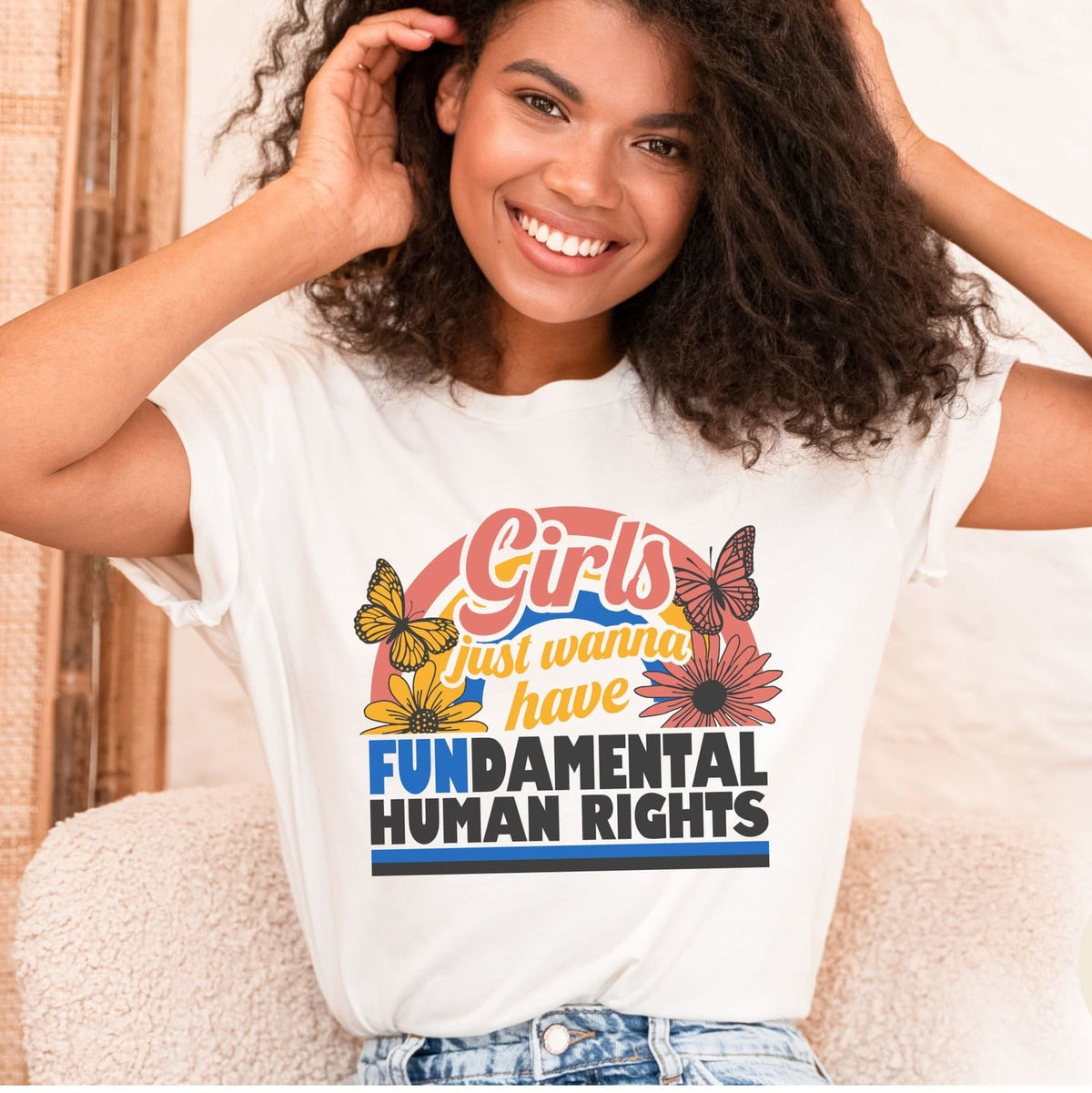 Woman wearing a white feminist t-shirt with a colorful graphic and text, sitting on a couch.