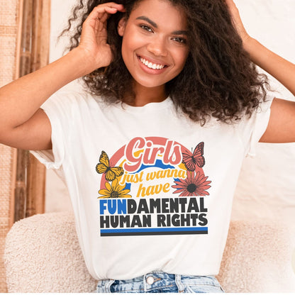 Woman wearing a white feminist t-shirt with a colorful graphic and text, sitting on a couch.