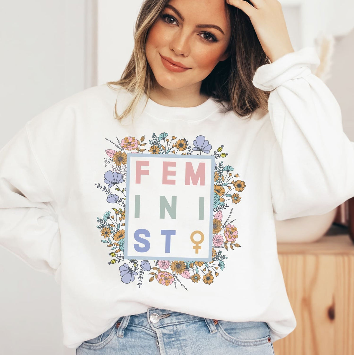 Person wearing a white sweatshirt with 'FEMINIST' and floral design.