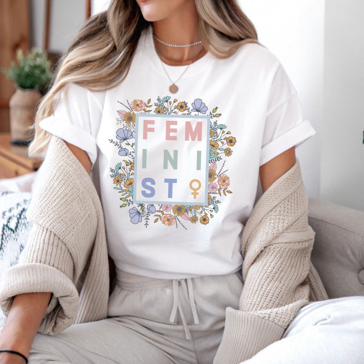 Person wearing a white t-shirt with floral 'FEMINIST' design in the center.