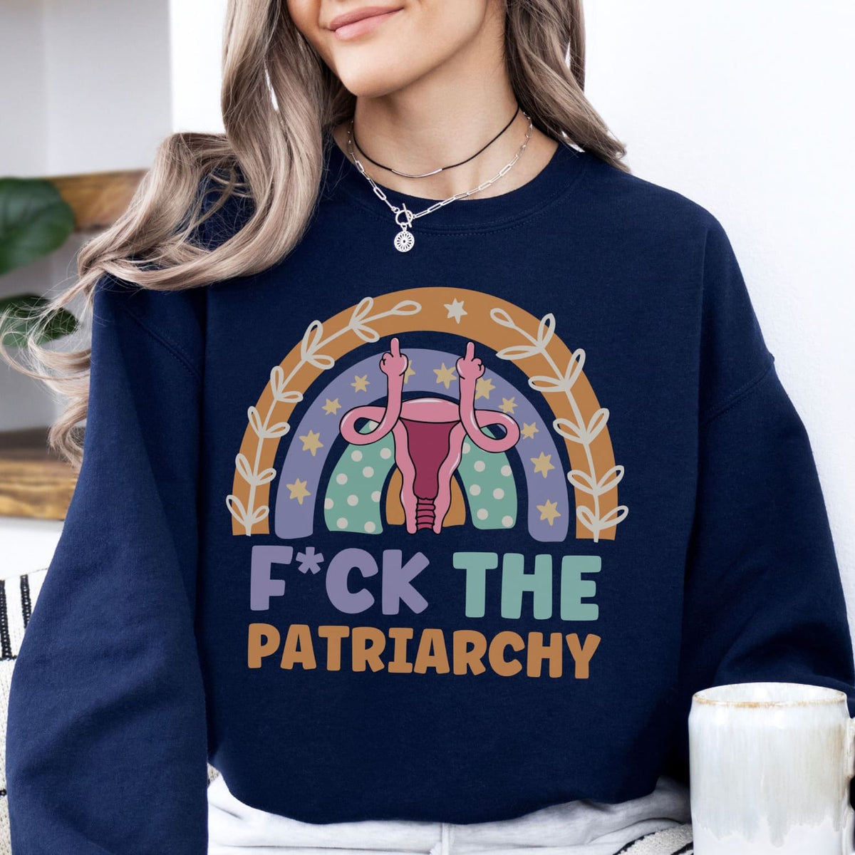 Person wearing a navy blue feminist sweatshirt with a rainbow design and 'F*CK THE PATRIARCHY' text.