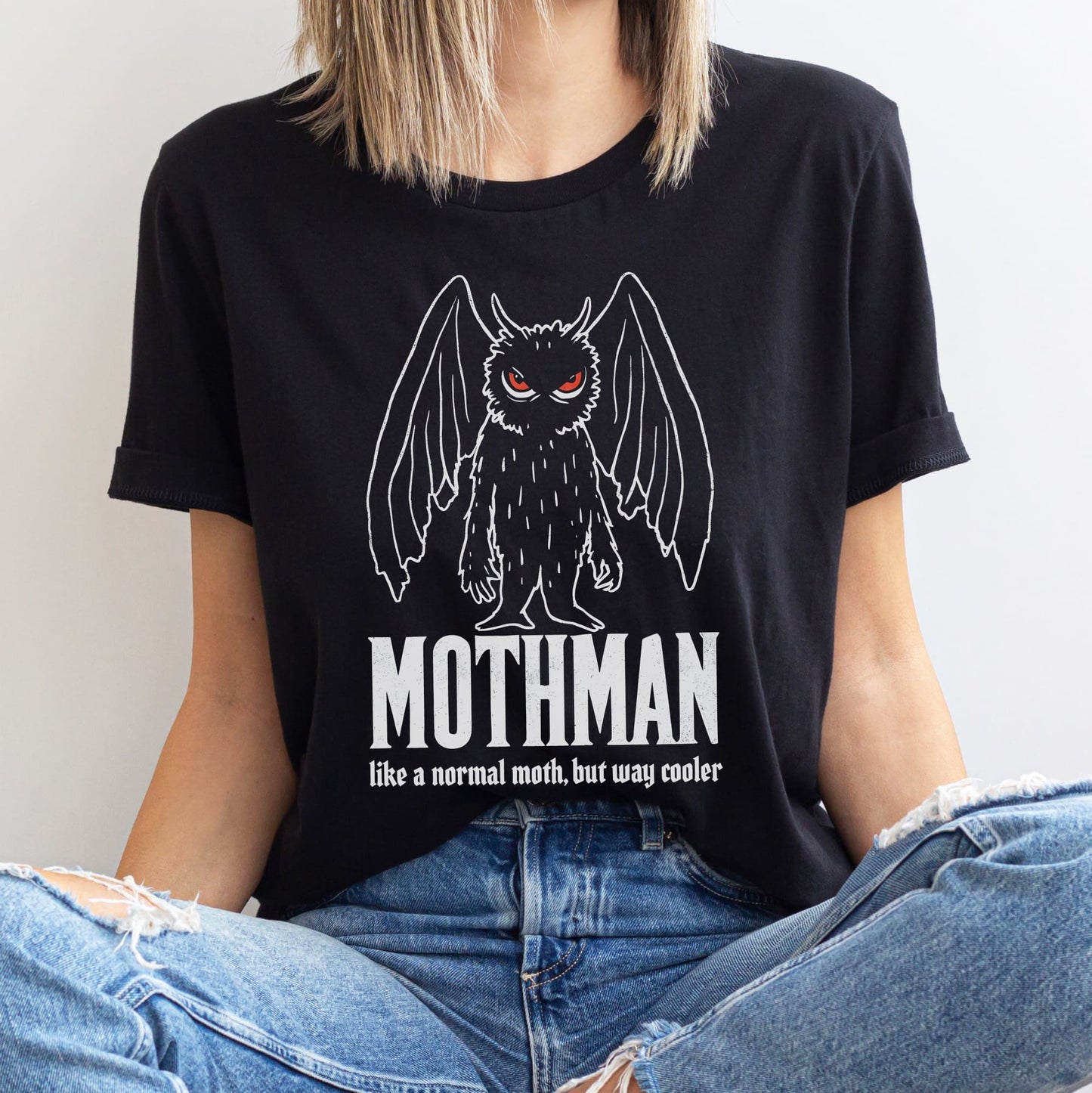 Person wearing a black t-shirt with Mothman graphic and text.
