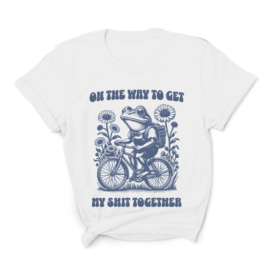 White t-shirt with a graphic of a frog riding a bike and text on a white background: Funny Neurodivergent Shirt, ADHD AuDHD Tee, Mental Health T-Shirt, Vintage Frog, Sarcastic Adult Humor, On The Way To Get My Shit Together