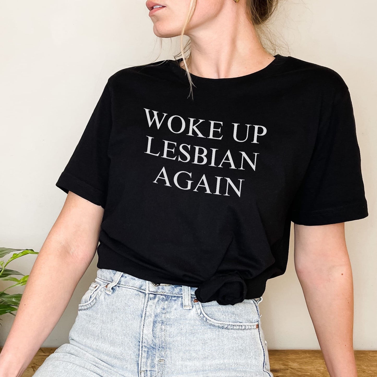 Person wearing a black t-shirt with 'Woke Up Lesbian Again' text.