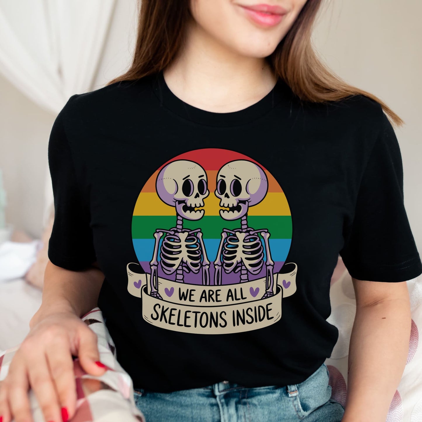 Person wearing a black t-shirt with a rainbow skeleton design and text: Pride Halloween Shirt, Funny Gay Skeletons On Rainbow Flag, LGBTQ Equality Diversity Human Rights Social Justice Tee, LGBT Gift For Queer