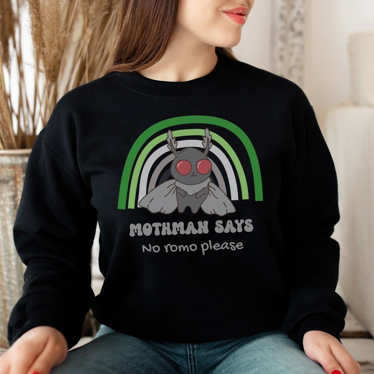 Person wearing a black aromantic sweatshirt with a graphic design of Mothman and text.
