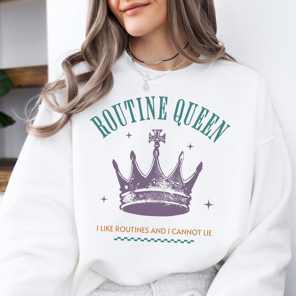 Person wearing a white sweatshirt with 'Routine Queen' text and crown graphic.