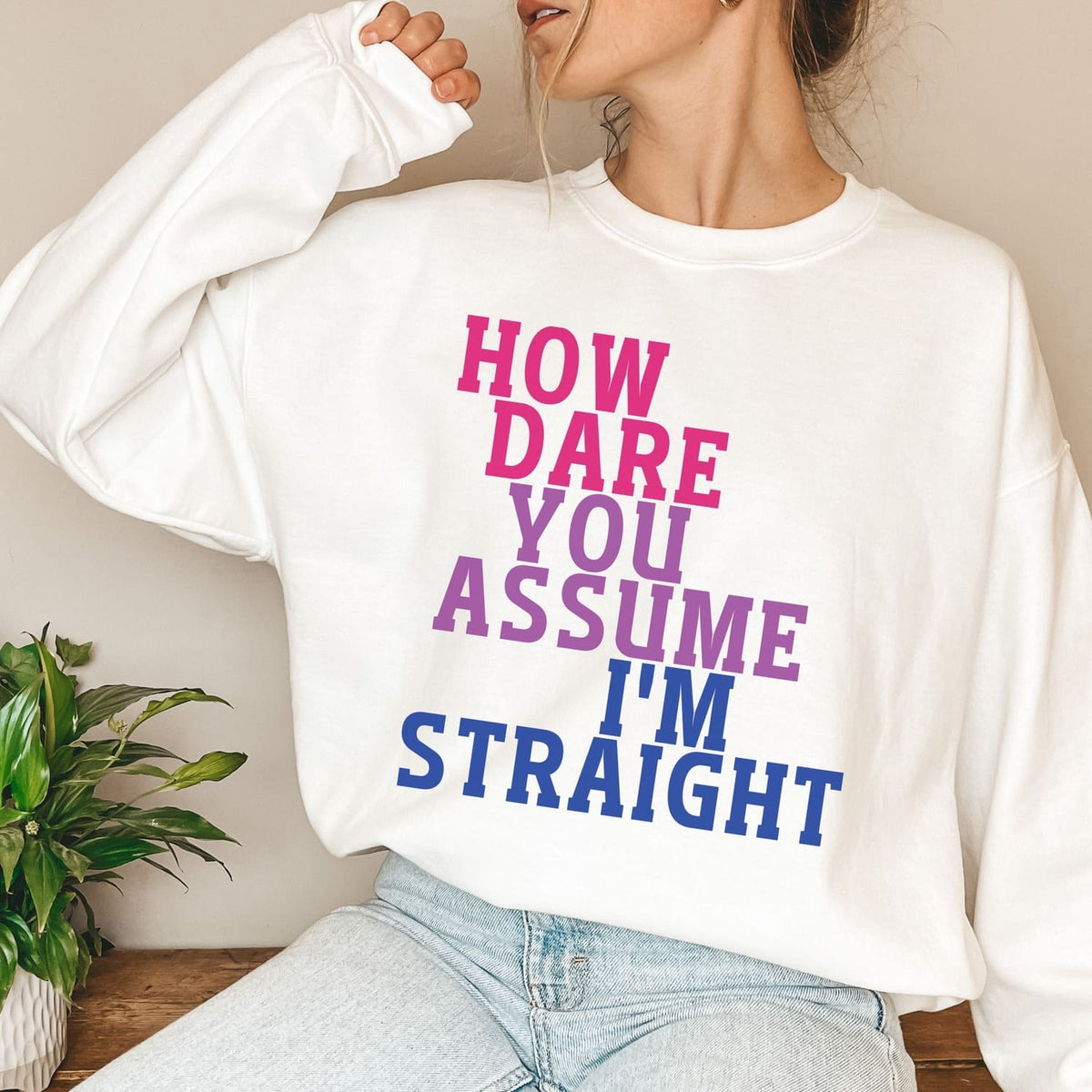 Person wearing a white bisexual sweatshirt with a colorful text design in a casual setting.