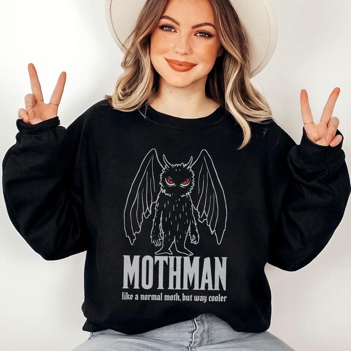 Person wearing a black sweatshirt with Mothman graphic and text