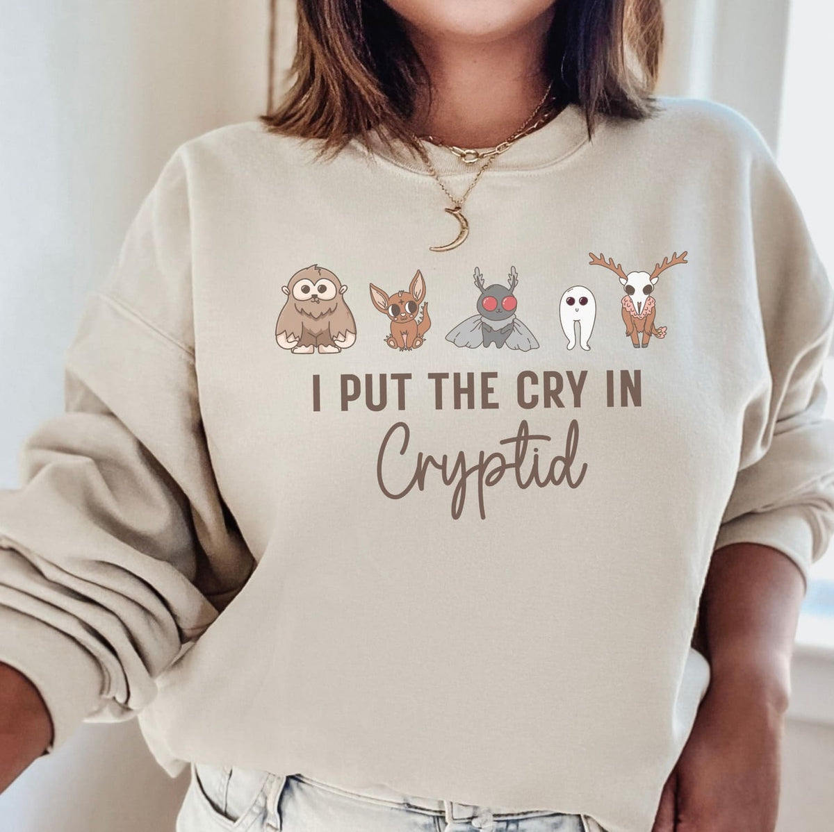 Beige sweatshirt with cryptid characters and text on a neutral background