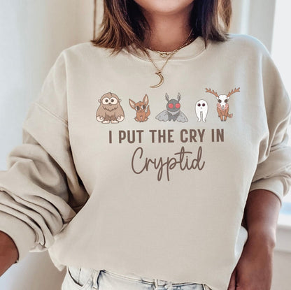 Beige sweatshirt with cryptid characters and text on a neutral background