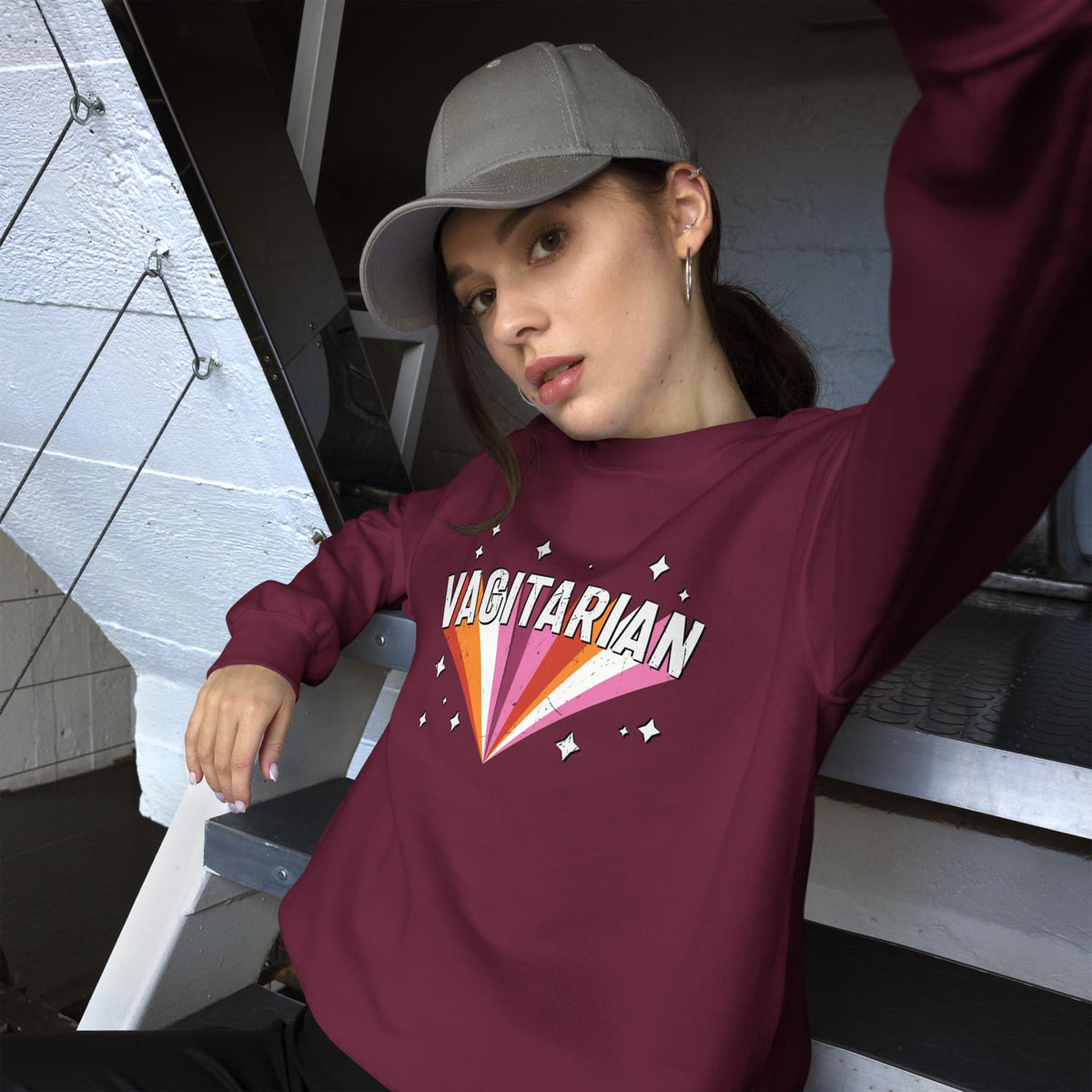 Lesbian wearing a maroon sweatshirt with 'VAGITARIAN' design, sitting on a staircase.
