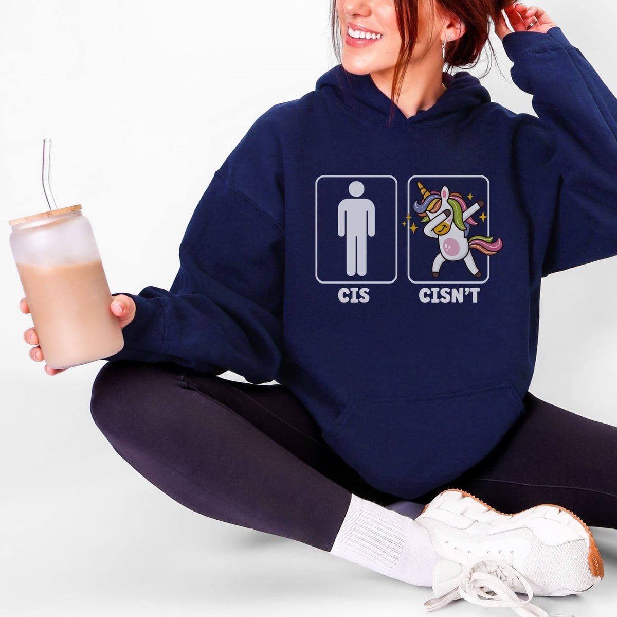 Person wearing a navy hoodie with a funny non cisgender graphic design, holding an iced coffee.