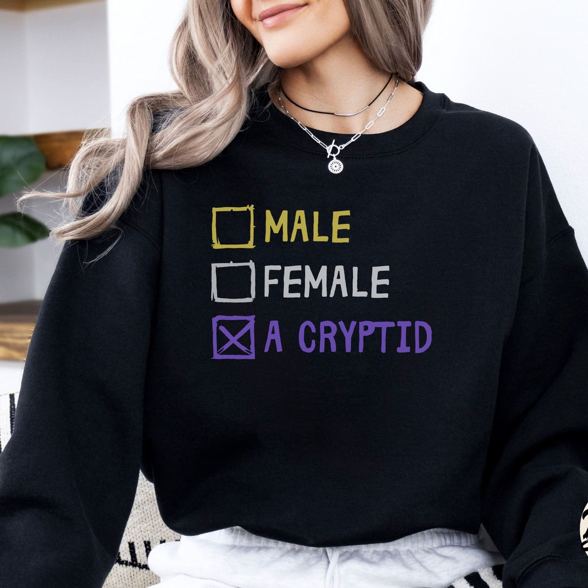 Person wearing a black nonbinary sweatshirt with gender options and 'A Cryptid' text.