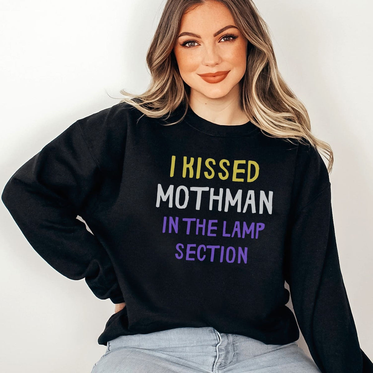 Person wearing a black nonbinary mothman sweatshirt with colorful text against a plain background