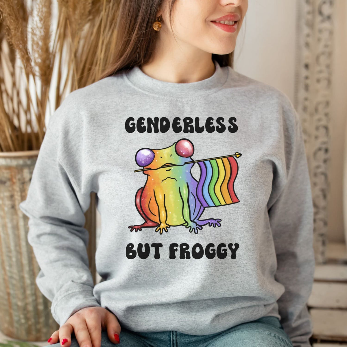 Person wearing a gray sweatshirt with a rainbow agender or nonbinary frog graphic and text.