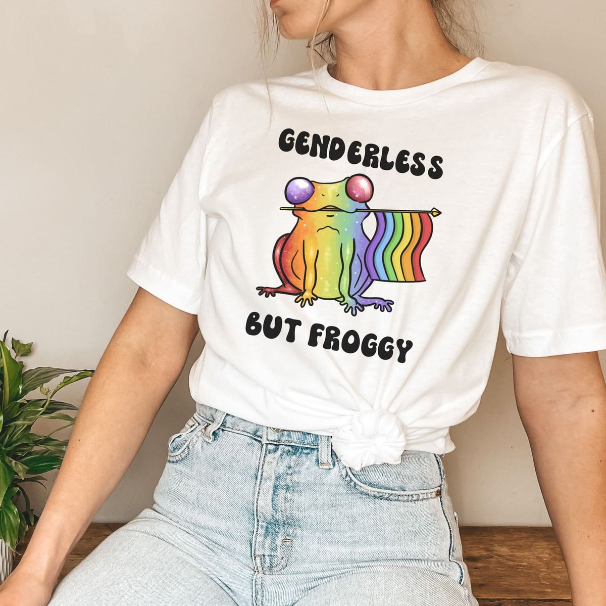 Person wearing a white t-shirt with a rainbow agender or nonbinary frog graphic and text.