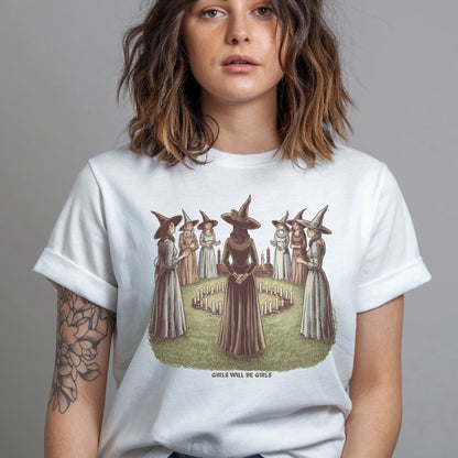 Person wearing a white t-shirt with a graphic design of women in witch costumes.