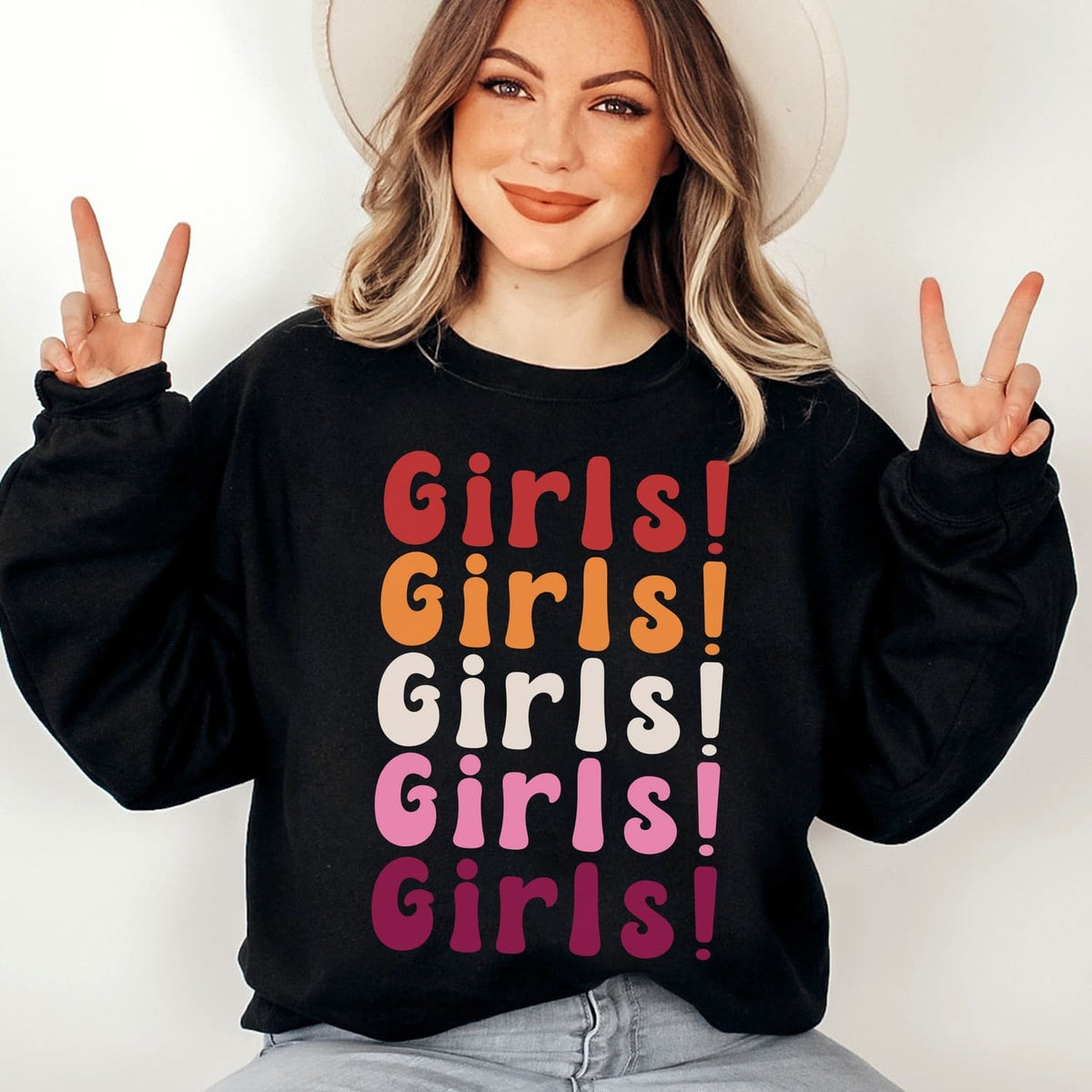 Person wearing a black sweatshirt with 'Girls! Girls! Girls!' text in lesbian sunset flag colors, making peace signs.