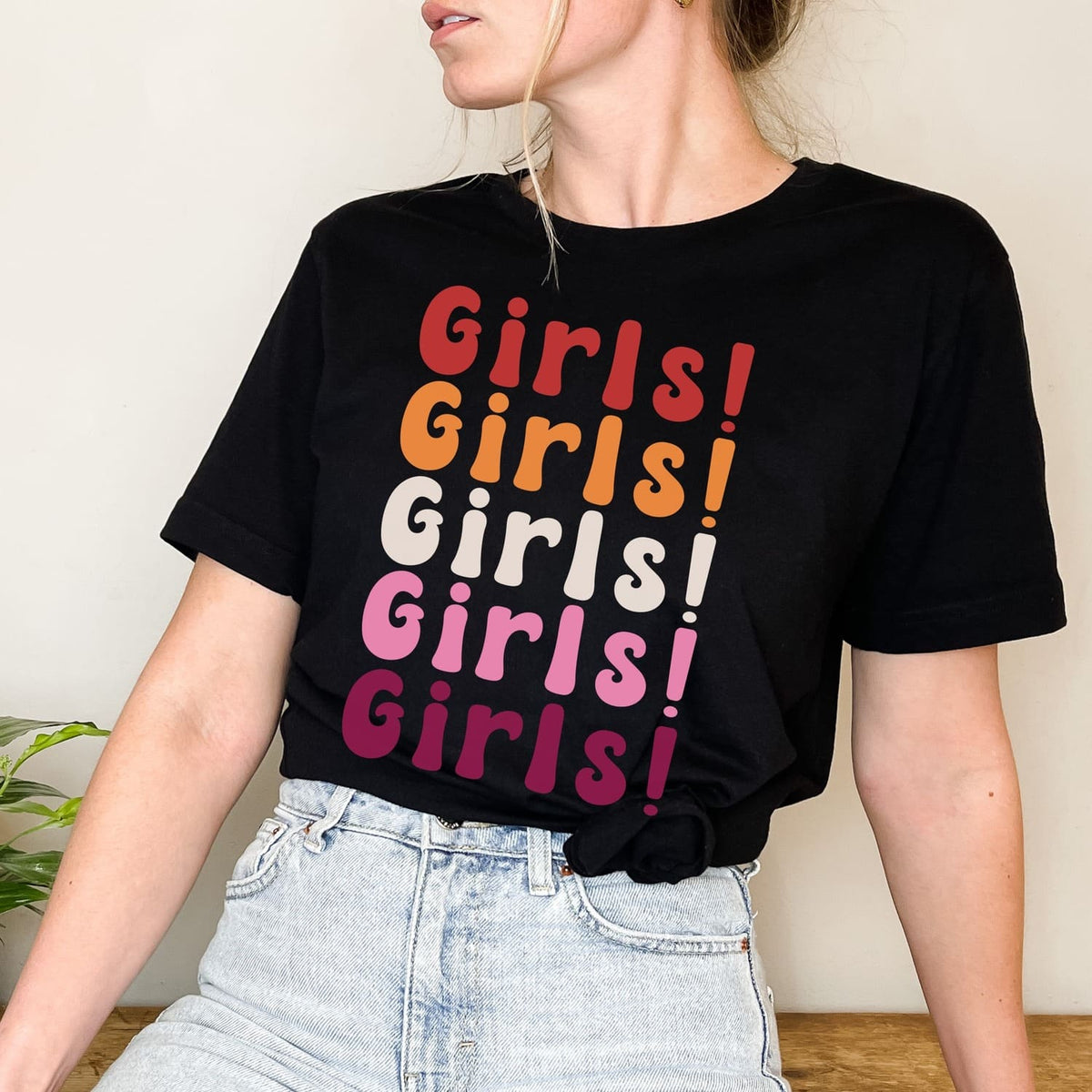 Person wearing a black t-shirt with  lesbian sunset flag colors ''Girls!' text design.