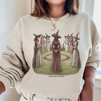 Person wearing a beige feminist sweatshirt with a graphic of witches and the text 'Girls Will Be Girls'.