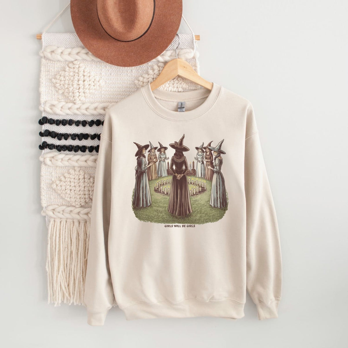 Beige feminist sweatshirt with graphic design on a hanger against a white wall.