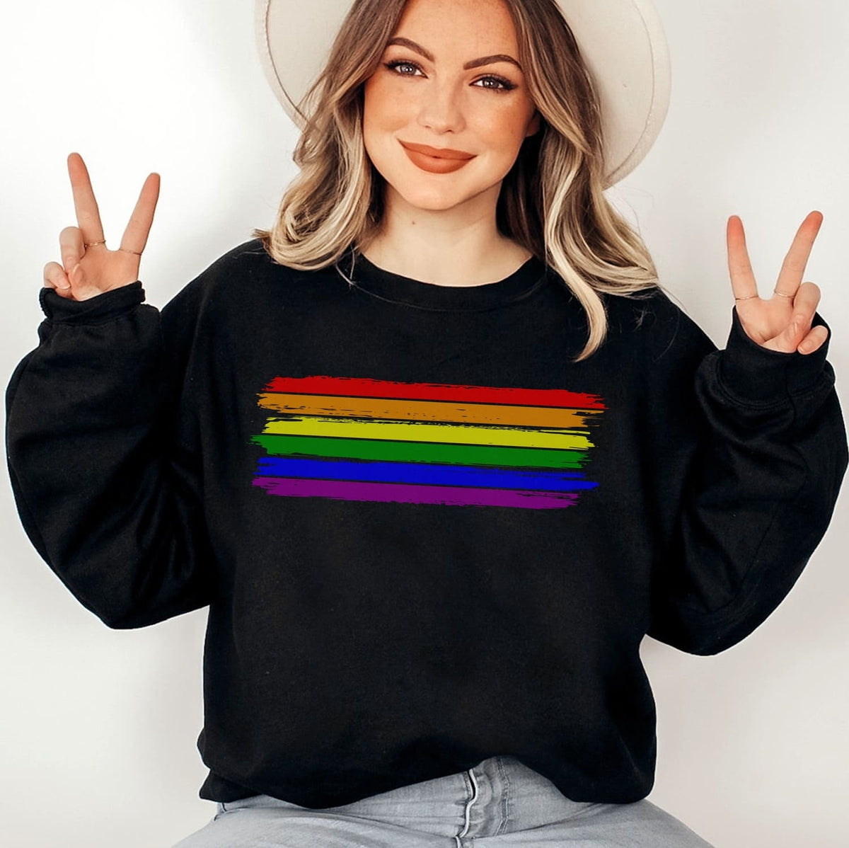 Person wearing a black lgbt pride sweatshirt with a rainbow stripe design, making peace signs.