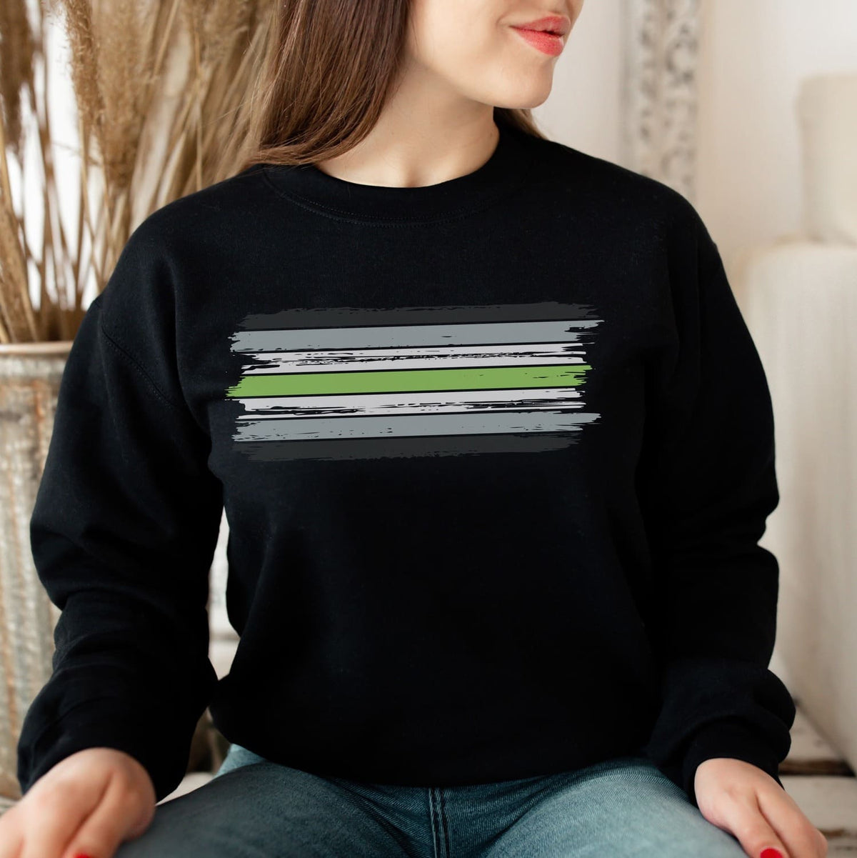 Person wearing a black agender sweatshirt with a graphic design sitting indoors.