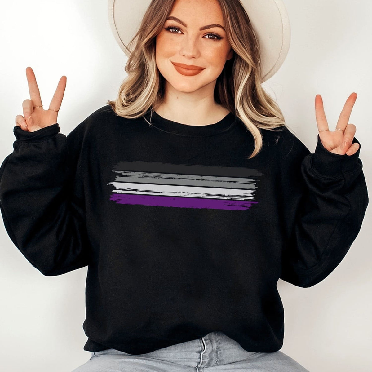 Person wearing a black asexual sweatshirt with a pride flag design, making peace signs.
