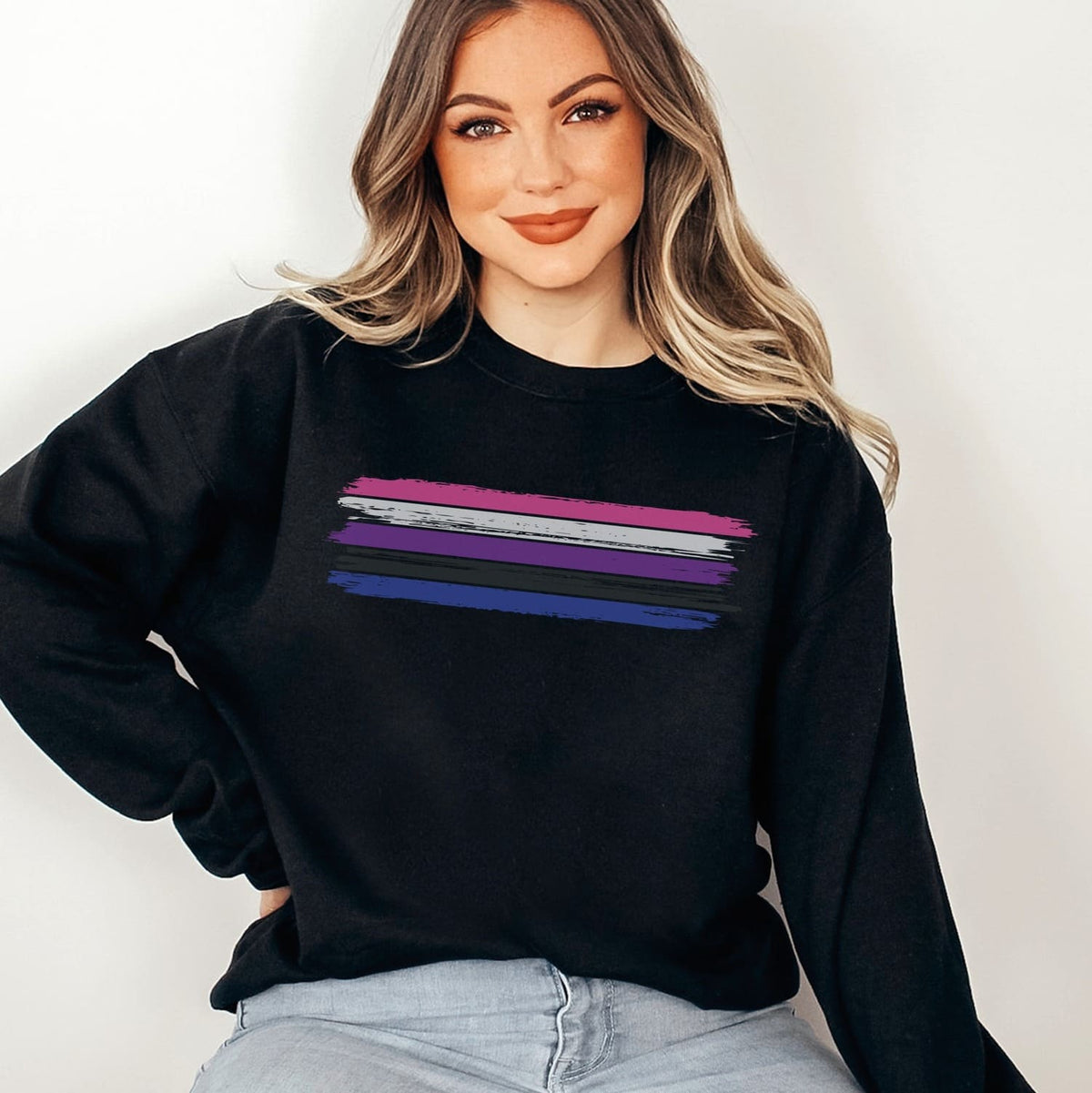 Person wearing a black genderfluid sweatshirt with rainbow stripes on a plain background