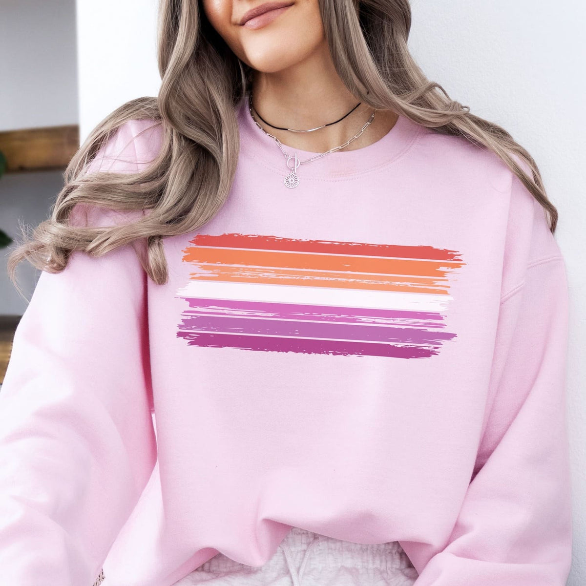 Person wearing a pink lesbian sweatshirt with a colorful design on a white background