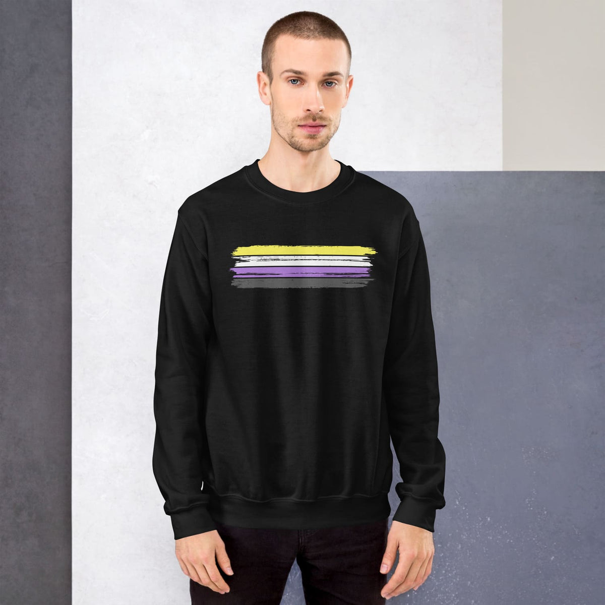 Man wearing a black sweatshirt with 'nonbinary grunge flag against a gray wall.
