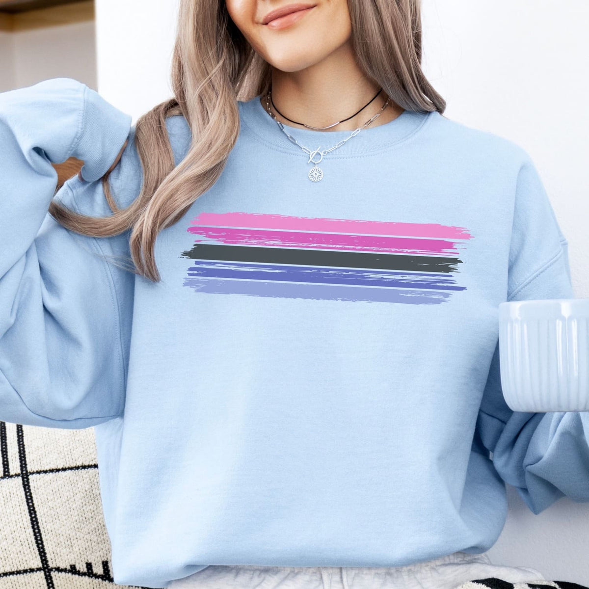 Person wearing a light blue omnisexual sweatshirt with colorful stripes, holding a white mug.