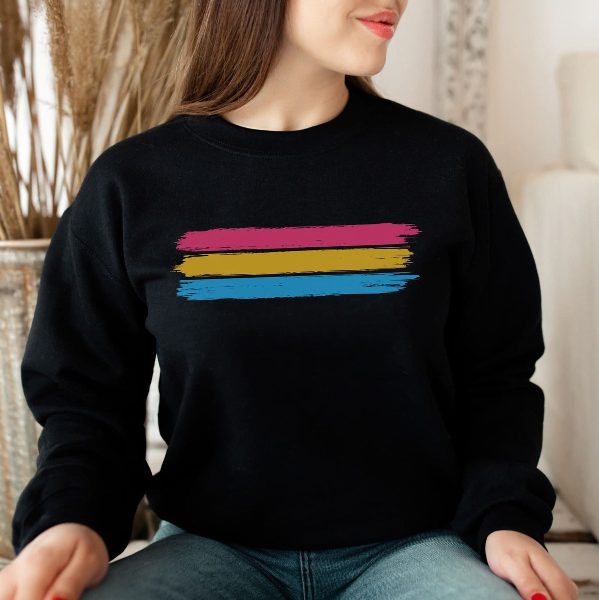 Person wearing a black pansexual sweatshirt with grunge flag stripes sitting indoors.