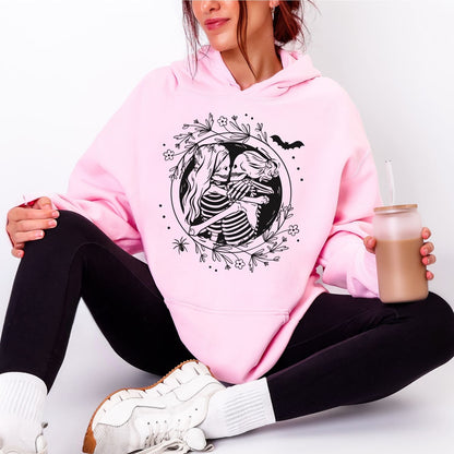 Person wearing a pink hoodie with a hugging lesbian skeleton couple design, sitting on a white background