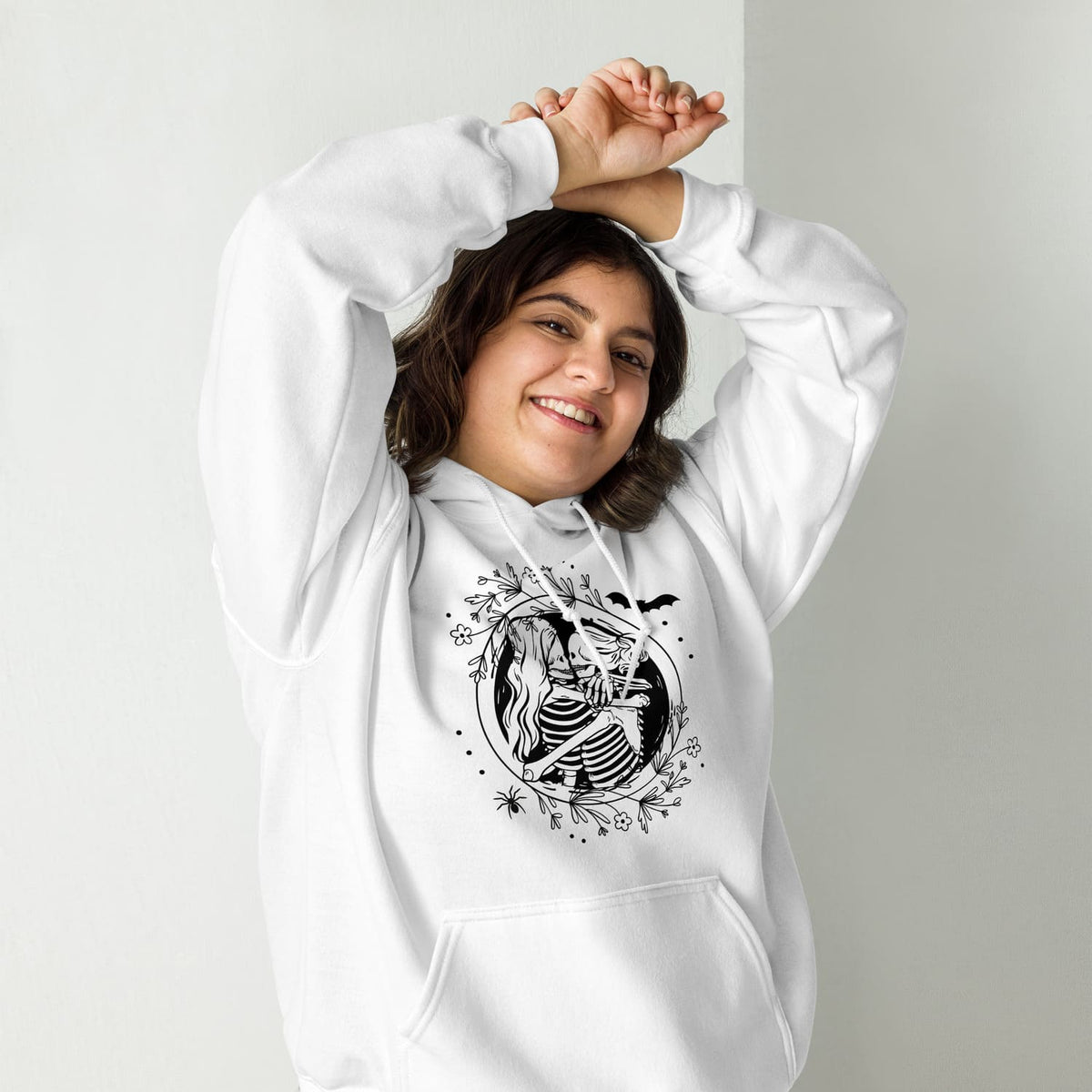 Person wearing a white hoodie with a hugging lesbian skeleton couple design on a plain background