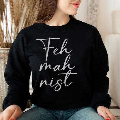 Person wearing a black feminist sweatshirt with 'Feh mah mist' text in a home setting
