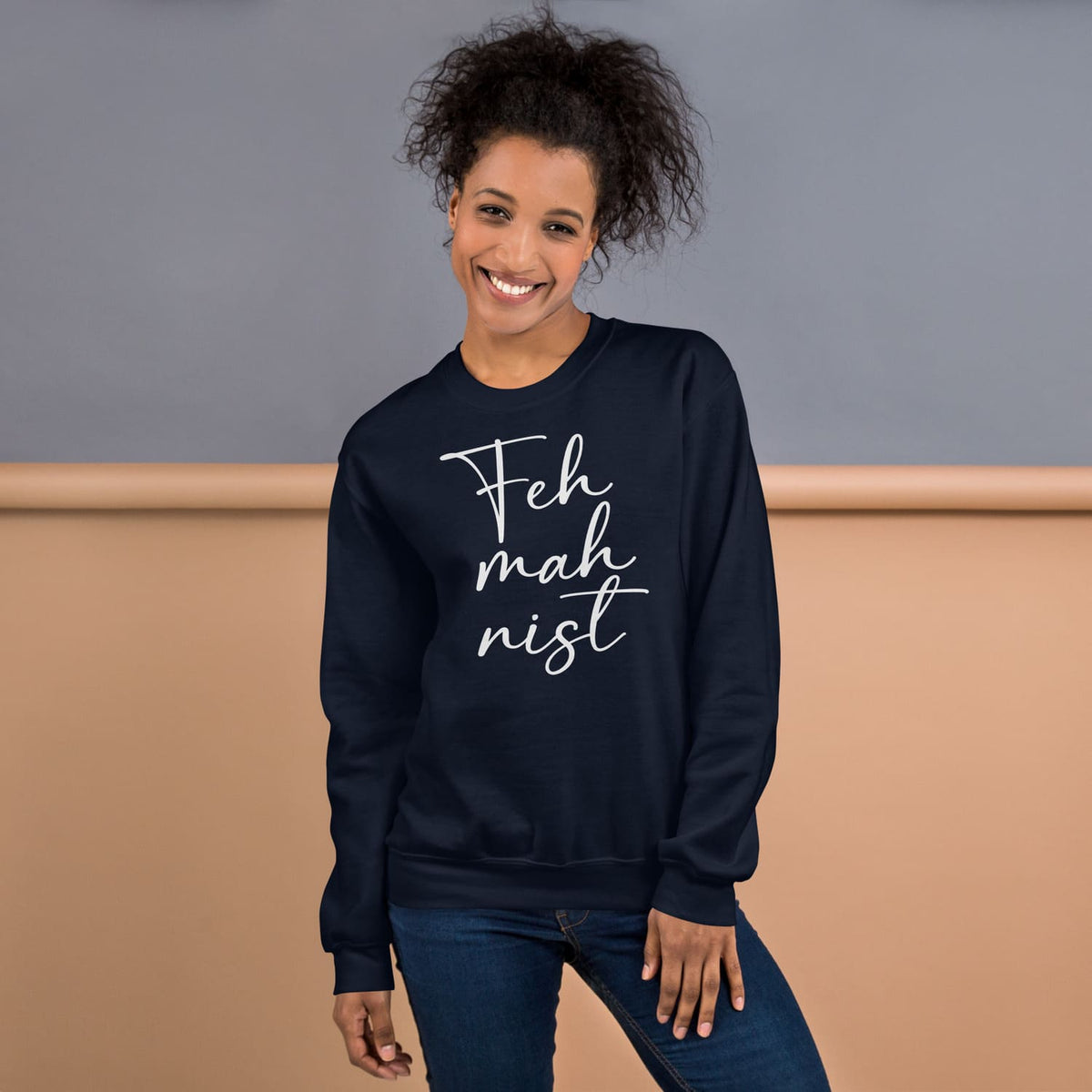 Woman wearing a navy blue feminist sweatshirt with 'Feh mah nist' text against a neutral background