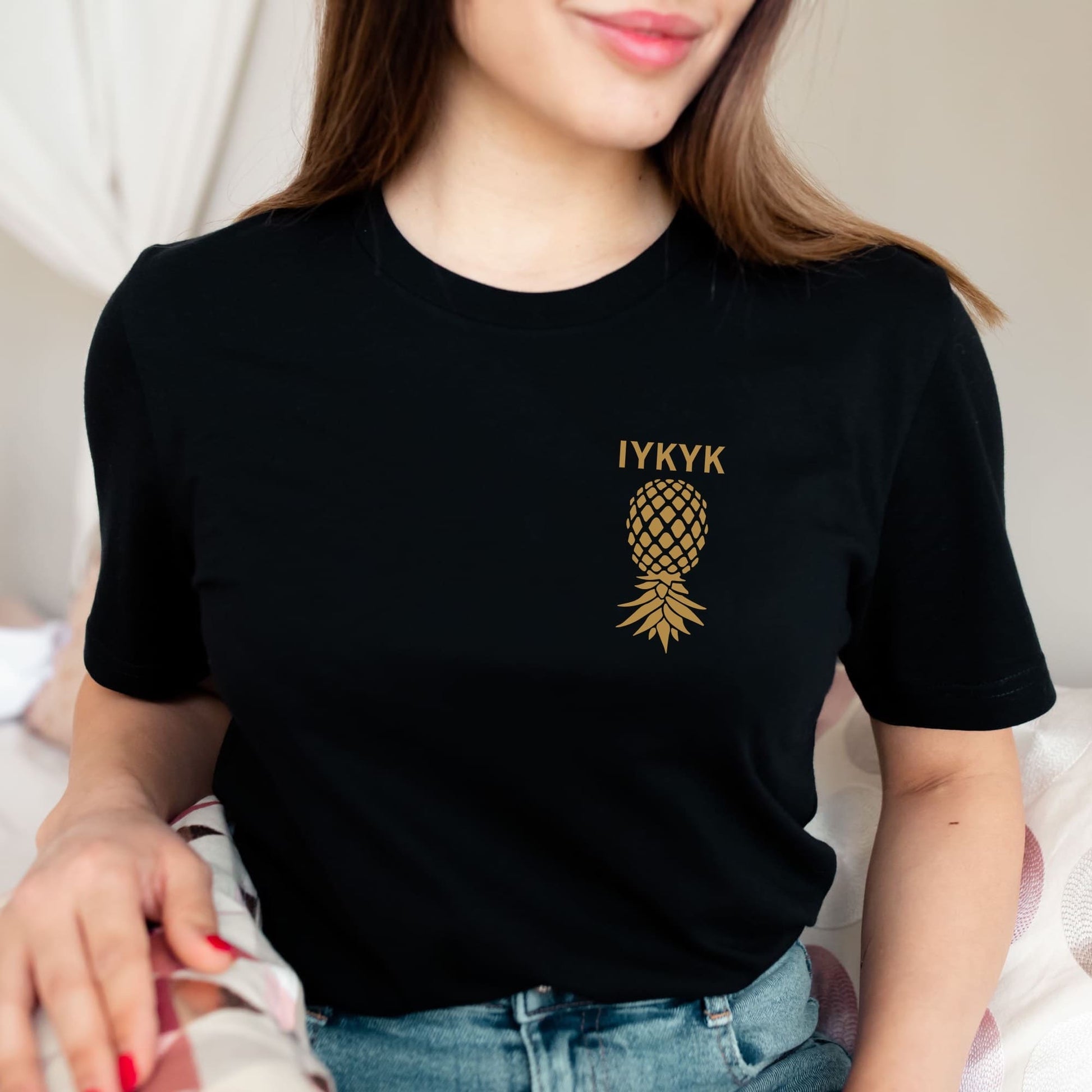 Person wearing a black t-shirt with a gold pineapple logo and text: Subtle Swingers Shirt, Upside Down Pineapple Pocket Design Tee, IYKYK T-Shirt, Discreet  Hotwife Tshirt, Gift For Non Monogamy Couples