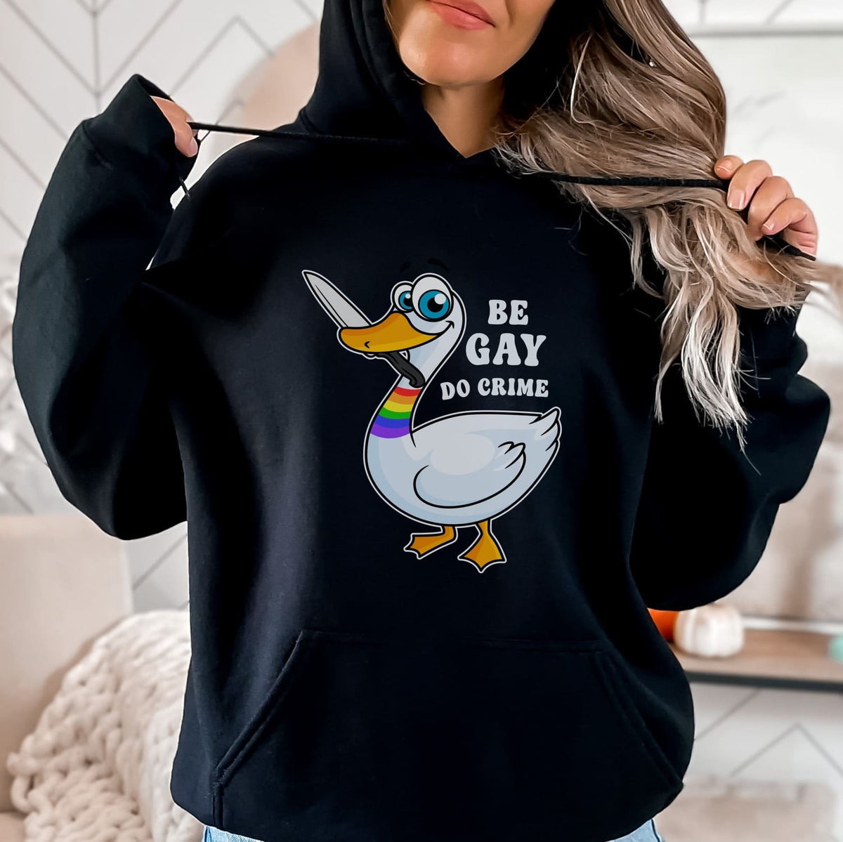Person wearing a black hoodie with a graphic of a duck and text 'Be Gay, Do Crime' in a casual setting.