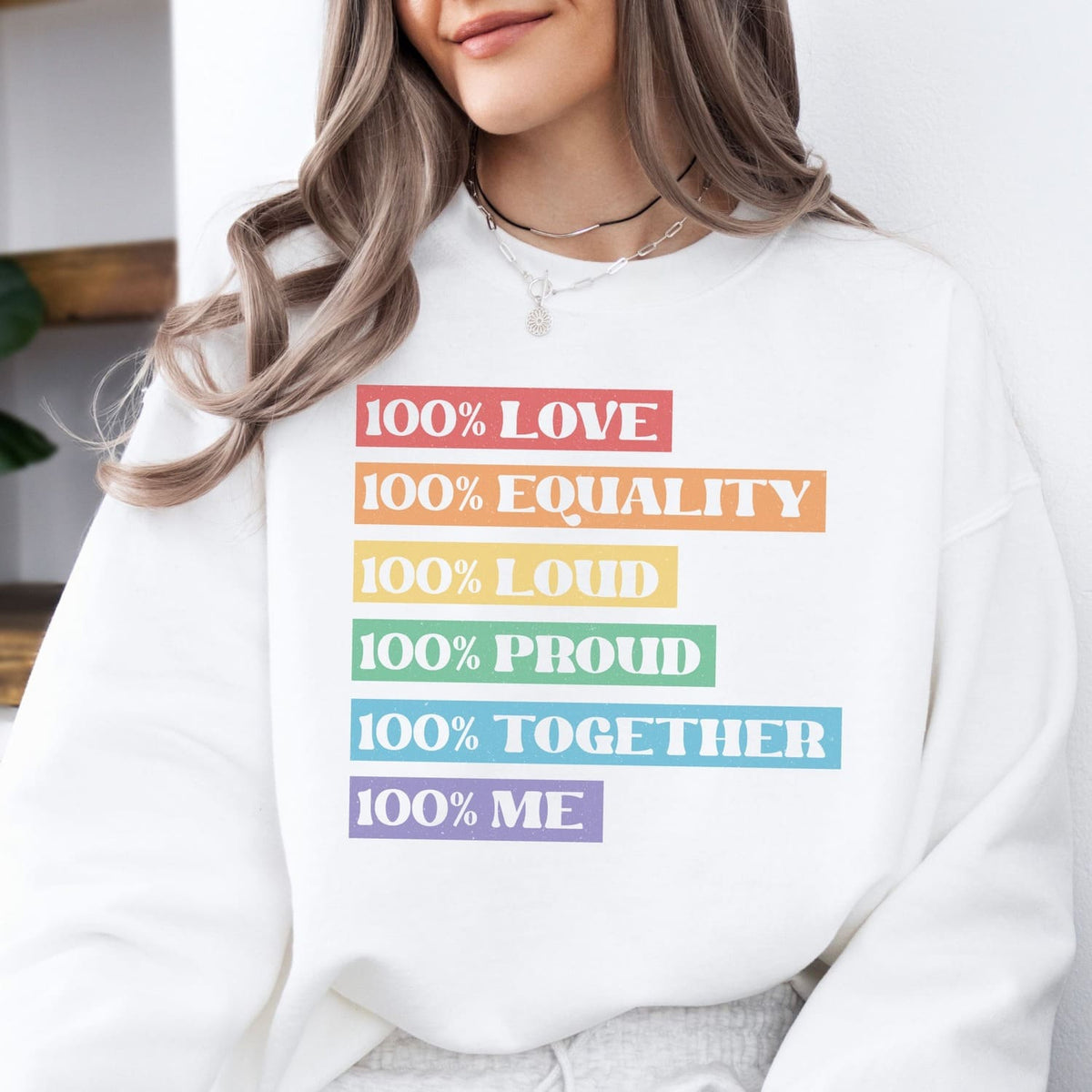 Person wearing a white lgbtq sweatshirt with colorful text about love, equality, and pride.