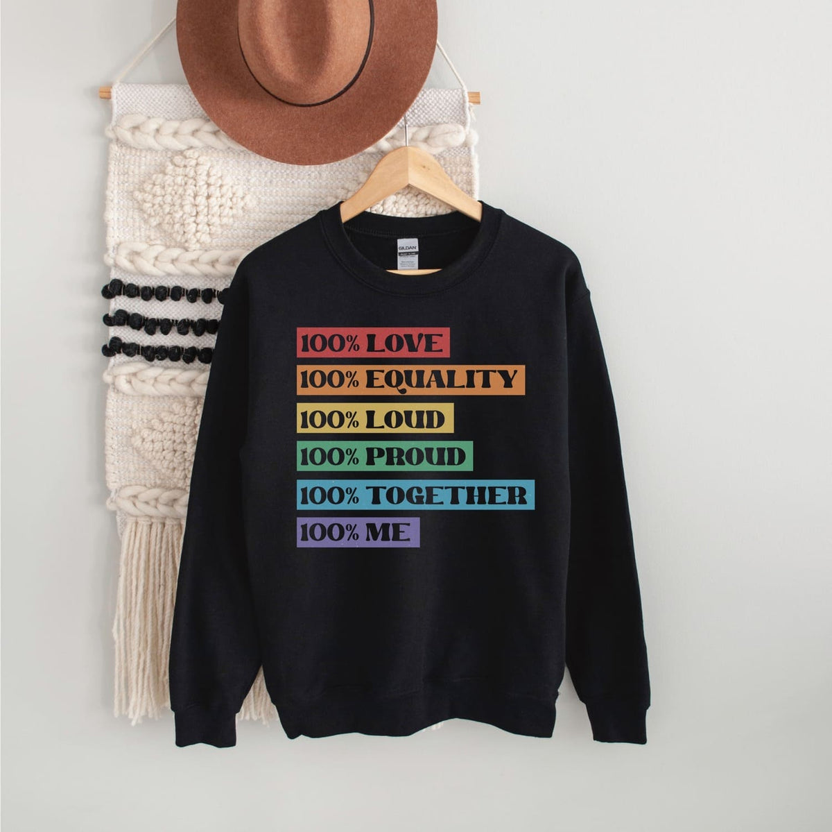 Black pride lgbt sweatshirt with colorful text on a hanger against a white wall.