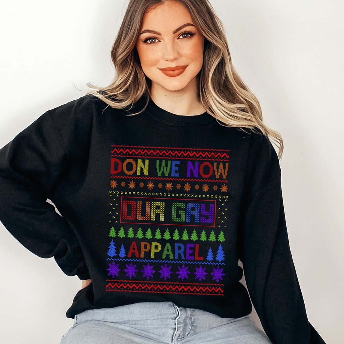 Person wearing a christmas pride sweater with rainbow text and patterns on a plain background