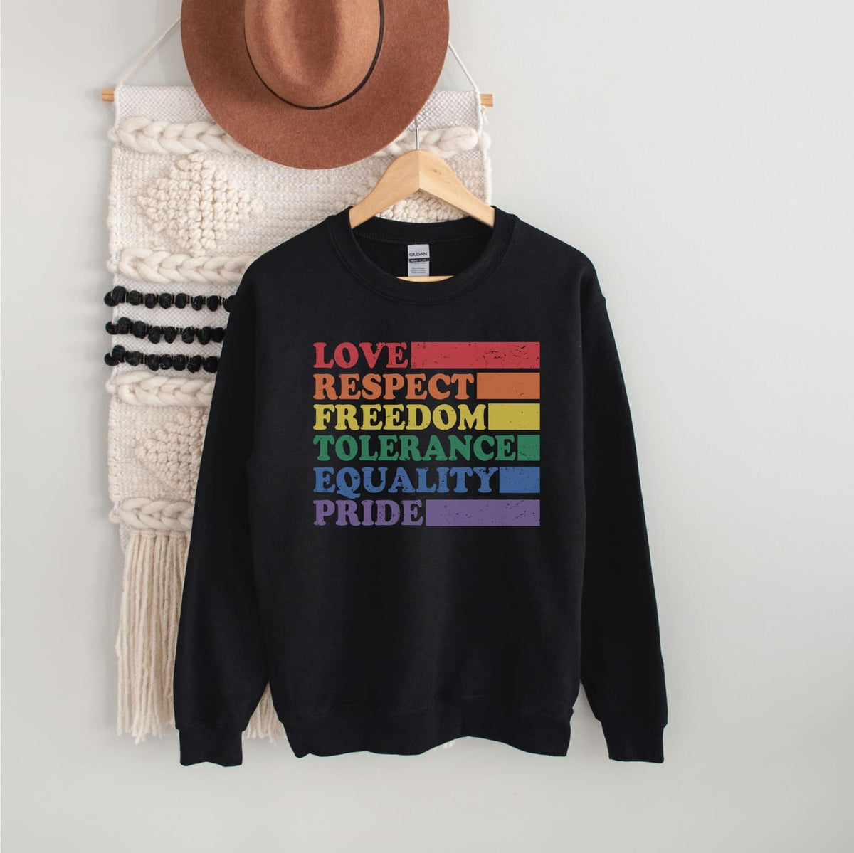 Black pride sweatshirt with LGBTQ rainbow-colored text on a hanger against a white wall.
