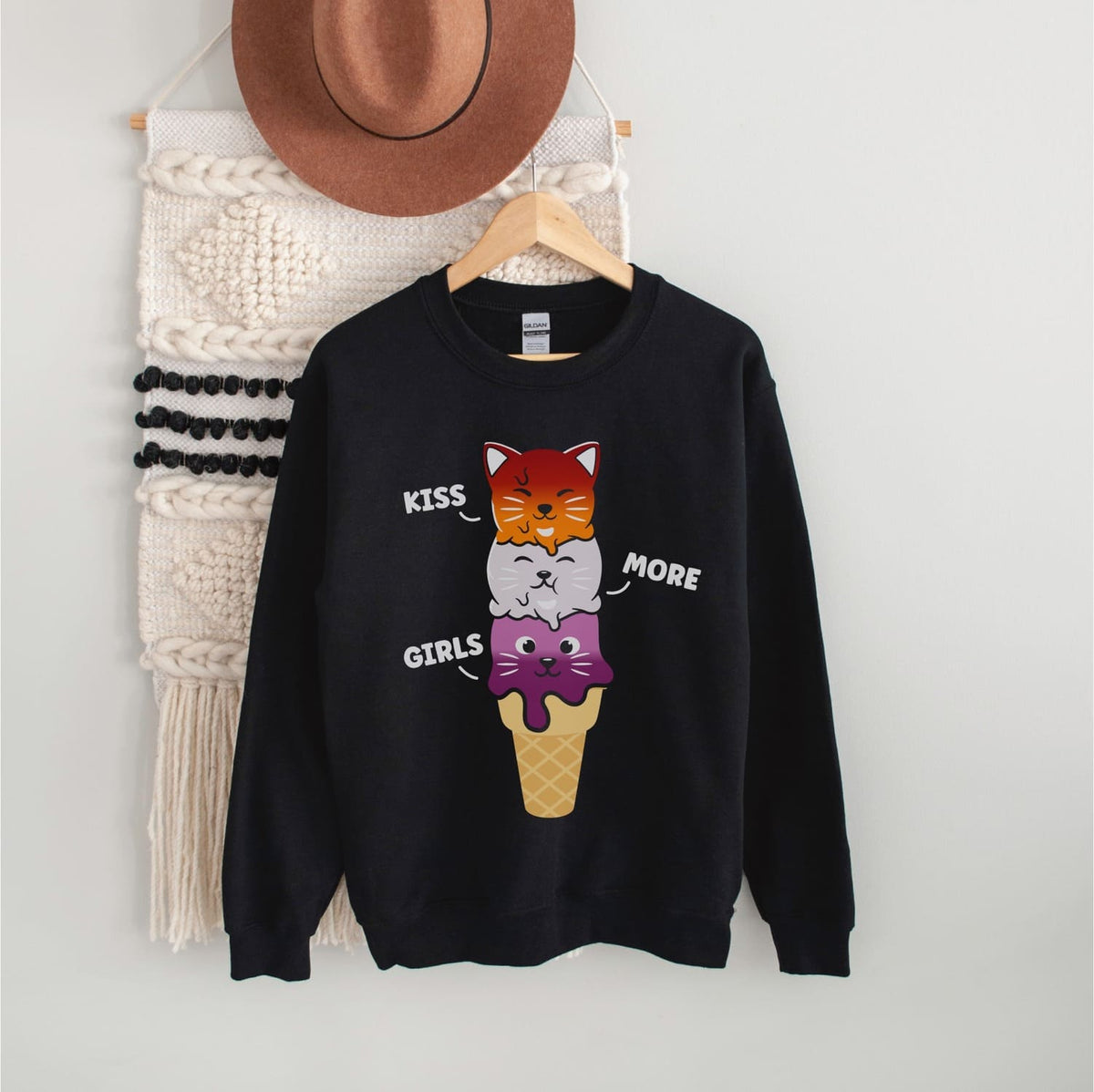 Black sweatshirt with lesbian cat design and text on a hanger against a white wall.