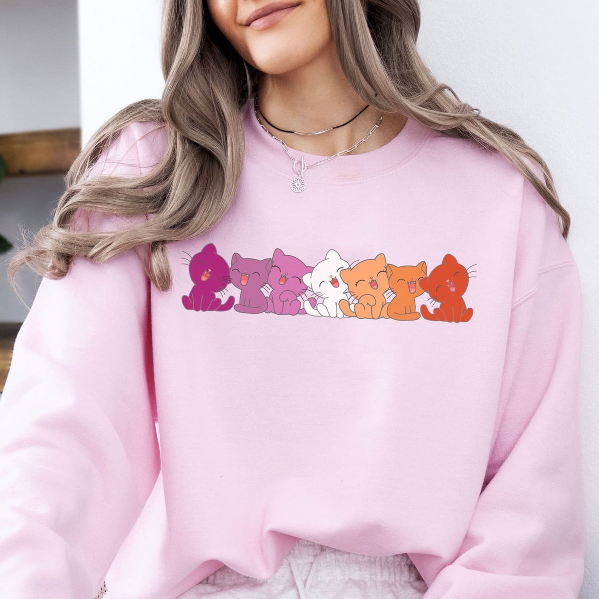 Person wearing a pink lesbian sweatshirt with colorful cat illustrations.